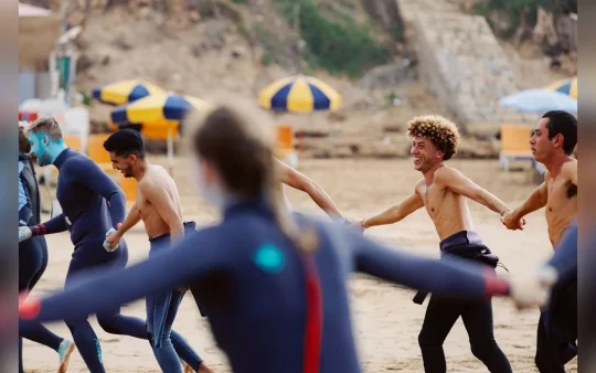 A serene view of Taghazout Bay, with surfers in the water and cozy accommodations nearby.