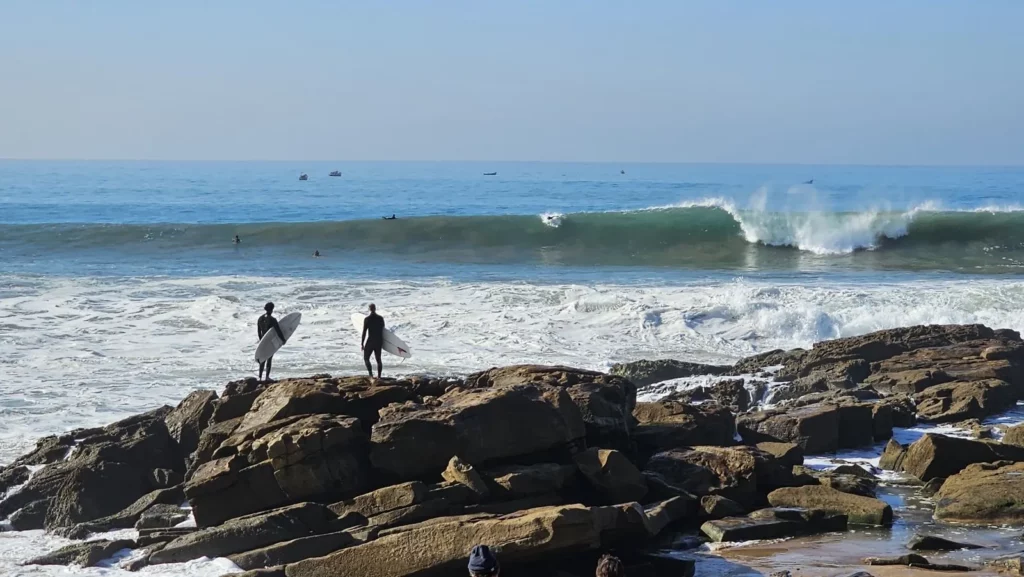 Surfing in Taghazout: two surfers on the rocks at Anchor Point as a long right-hand wave breaks