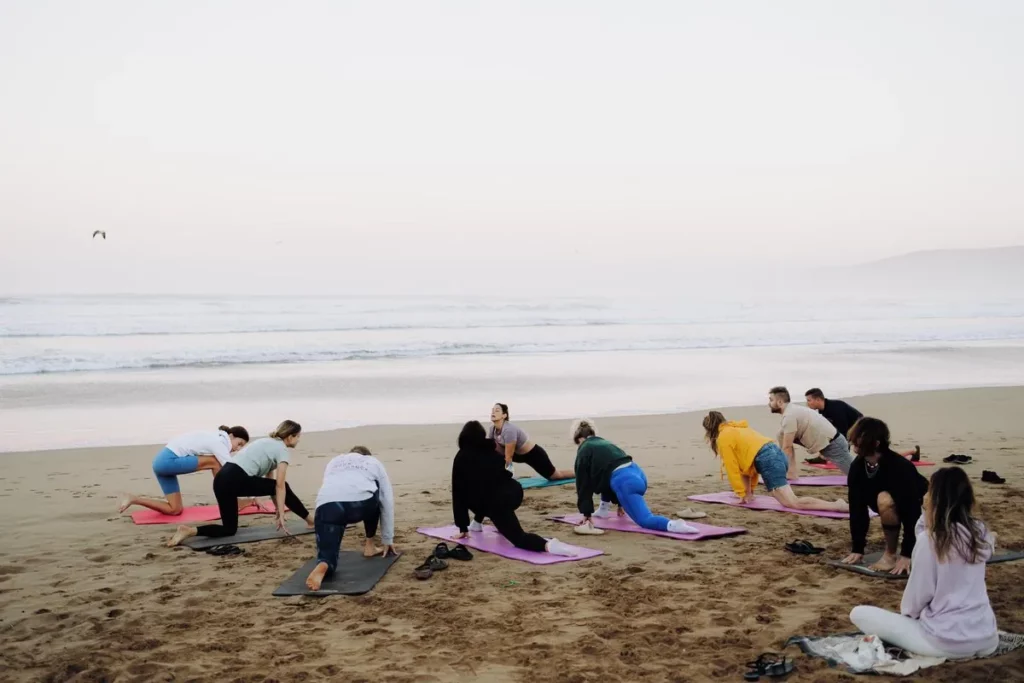 Surf camp guests doing yoga on the beach at sunrise in Taghazout Bay