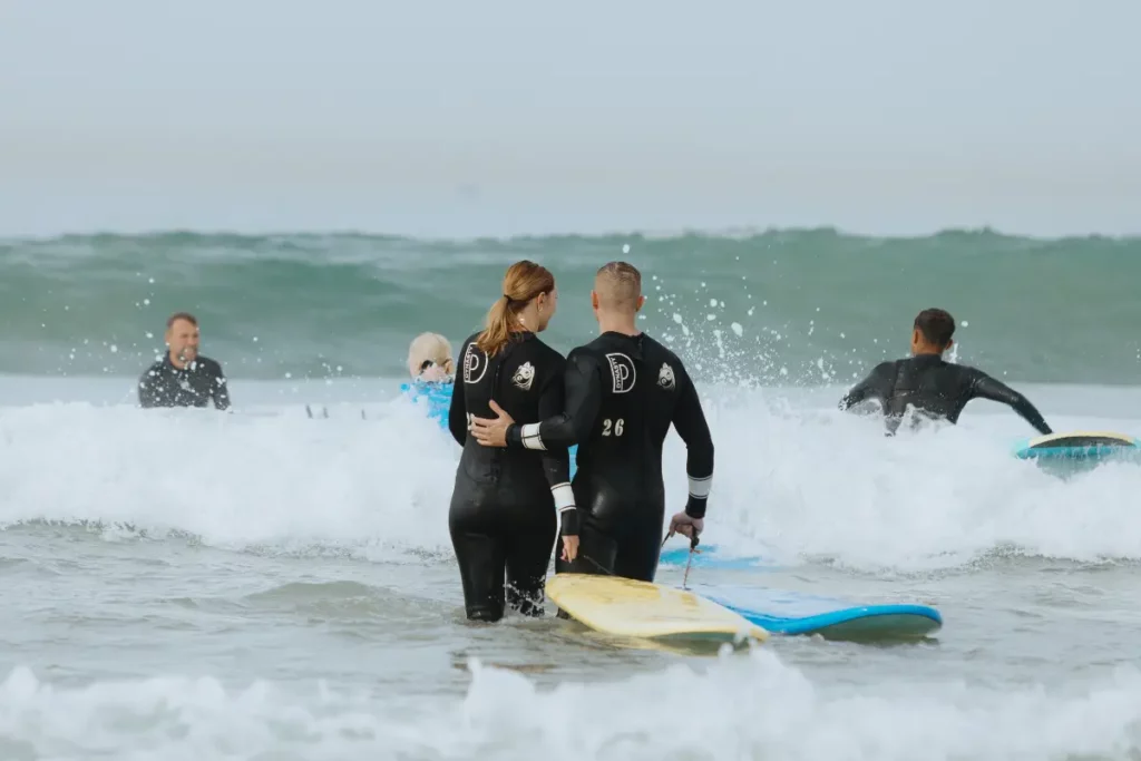 Couple in wetsuits walking into the waves with their boards for a surf lesson in Taghazout