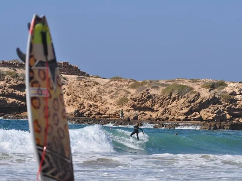 Surfer riding a wave at Devil's Rock beach in Tamraght with a surfboard in the foreground