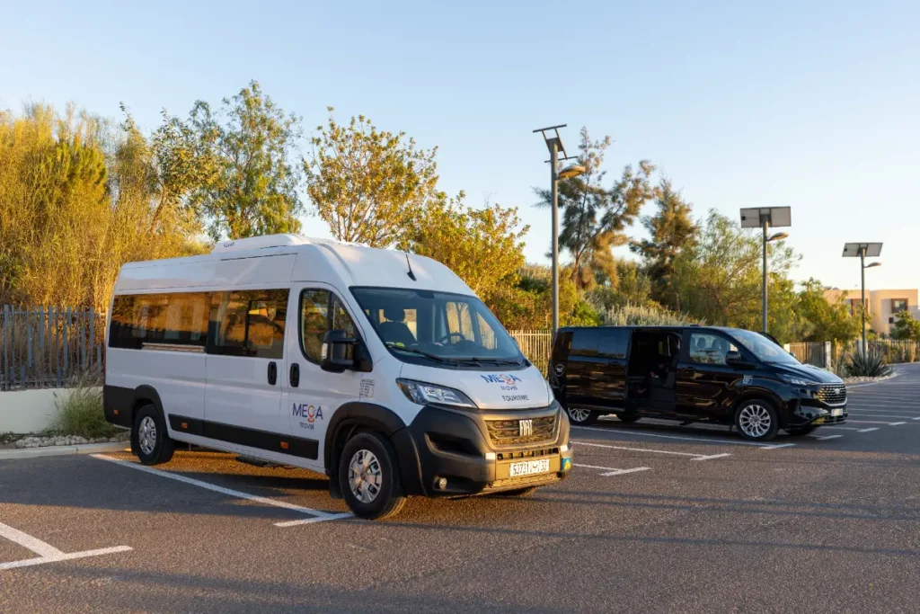 Vår vita minibuss och en svart van parkerade i solen, som används för flygplatstransfers och resor till surfplatserna i Taghazout