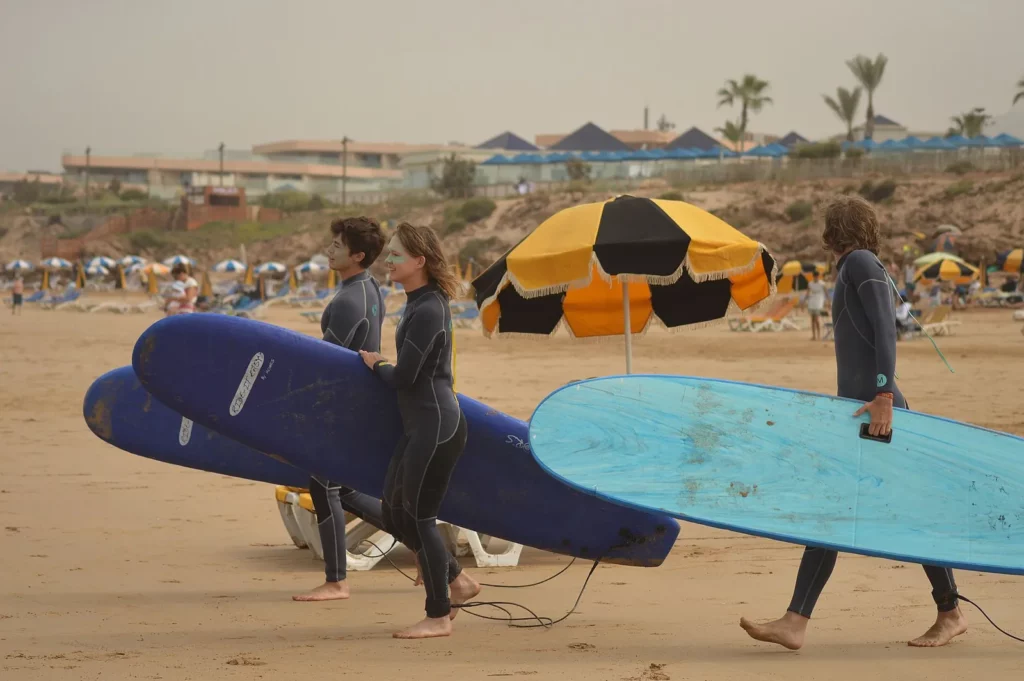Surf students carrying soft-top surfboards on the beach in Tamraght, Morocco